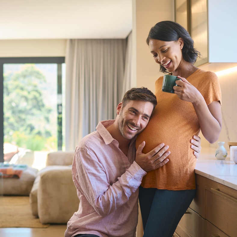 Loving Multi-Racial Couple With Pregnant Woman And Man Listening To Baby Heartbeat At Home